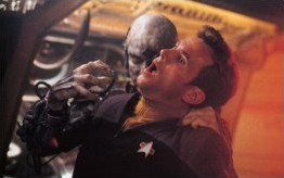 A hapless Starfleet redshirt (only, his shirt is mustard this time!) is seized by a scowling Borg drone, just prior to being assimilated via the new injection tube method.
